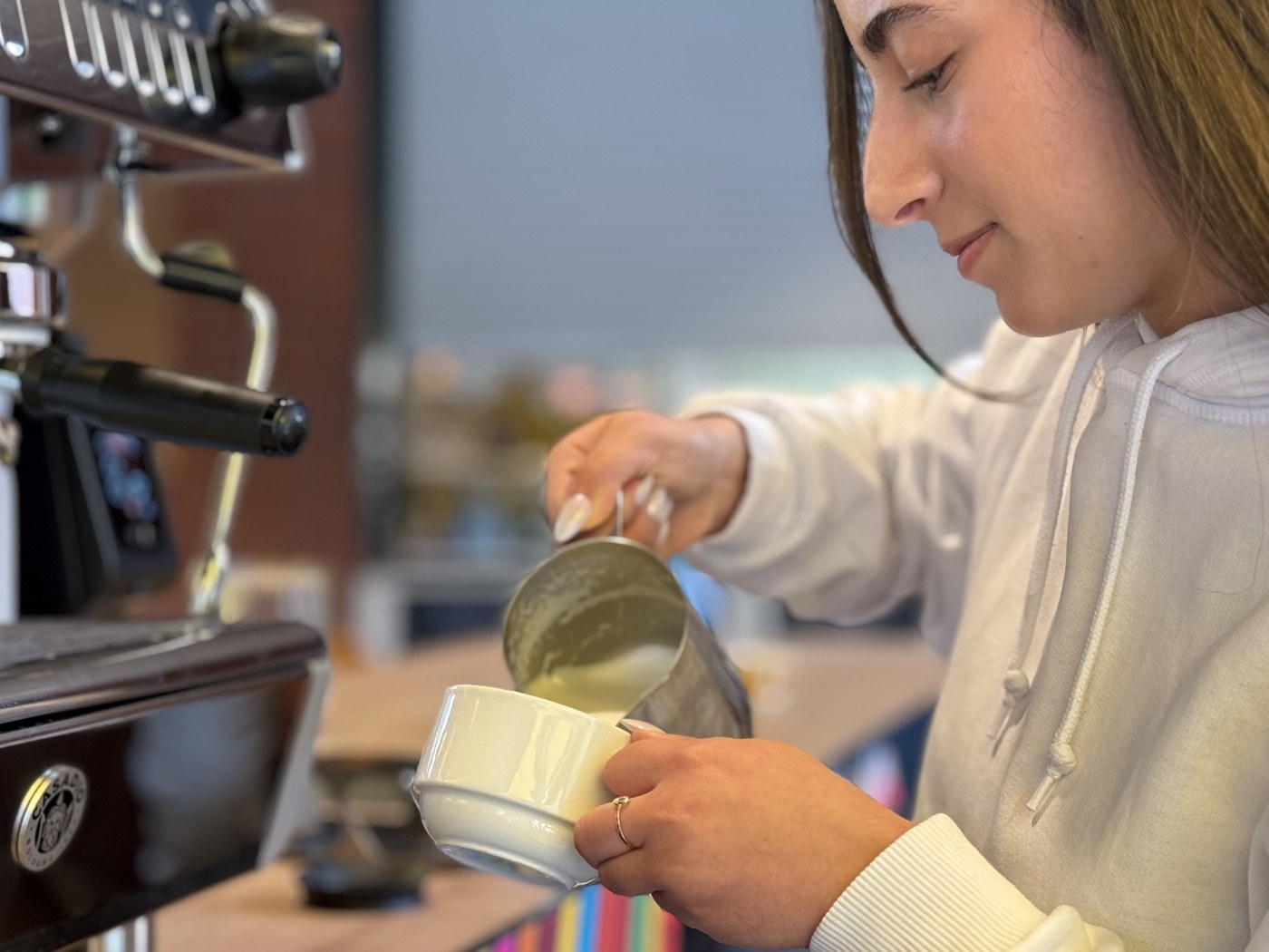 Eine junge Barista gießt an einer Espressomaschine Milchschaum in eine Tasse