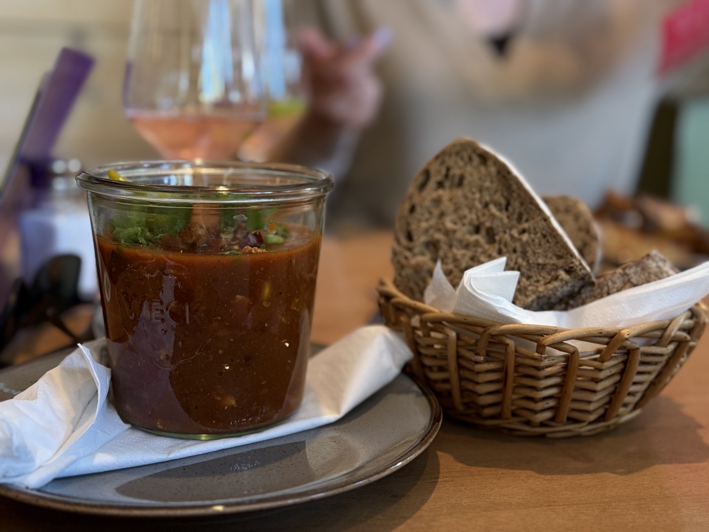 Ein Glas Gazpacho neben einem Brotkorb mit dunklem Bauernbrot auf einem Restauranttisch